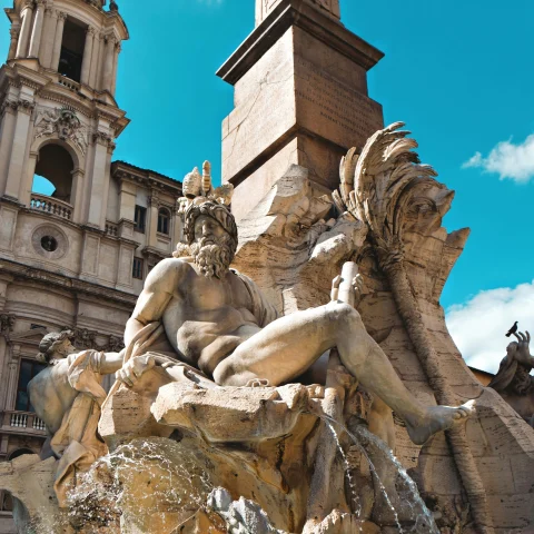Piazza Navona, with a fountain sculpture in front of an ancient building on a clear blue day, one of the attractions in Rome, Italy.