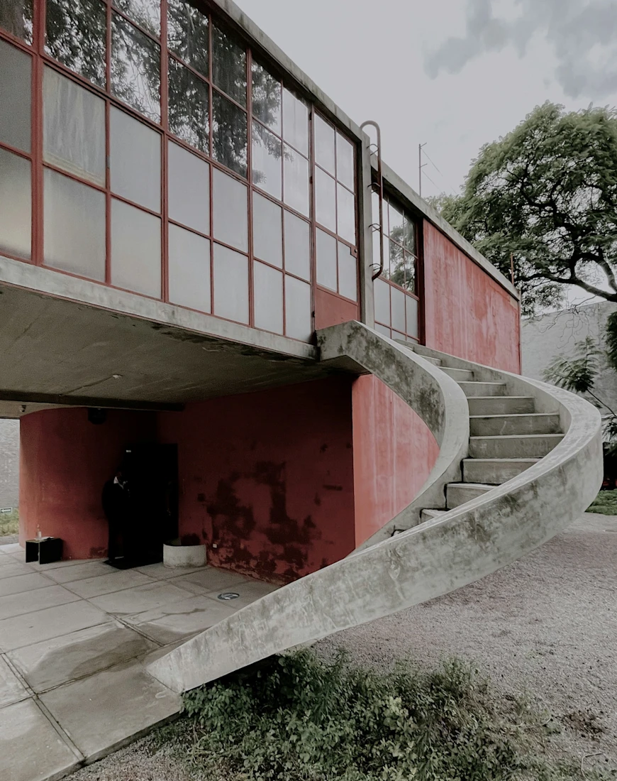 the exterior of a red building with a window wall and a spiral concrete staircase