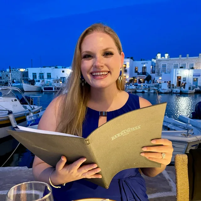 Rachel in a blue dress holding a menu in the evening.