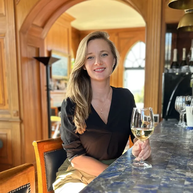 Travel Advisor Marielle Velander with a black shirt, holding a glass of white wine at a bar