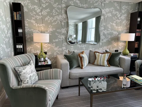 The sitting area of a suite at Brown's Hotel, London with gray and white flowery wallpaper, gray sofas with cushions and gray carpet.