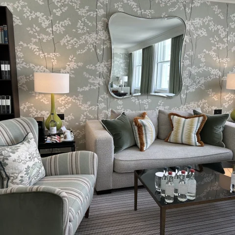 The sitting area of a suite at Brown's Hotel, London with gray and white flowery wallpaper, gray sofas with cushions and gray carpet.