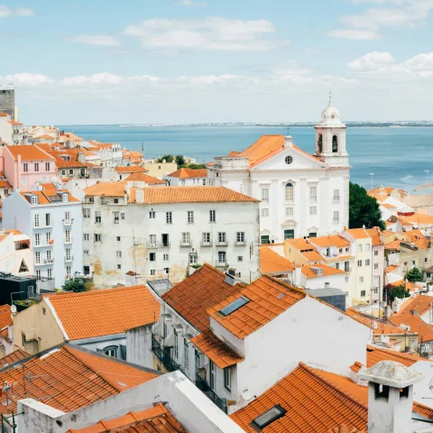 An aerial view of the landscape and architecture of orange roof houses in Lisbon with the ocean in the distance.