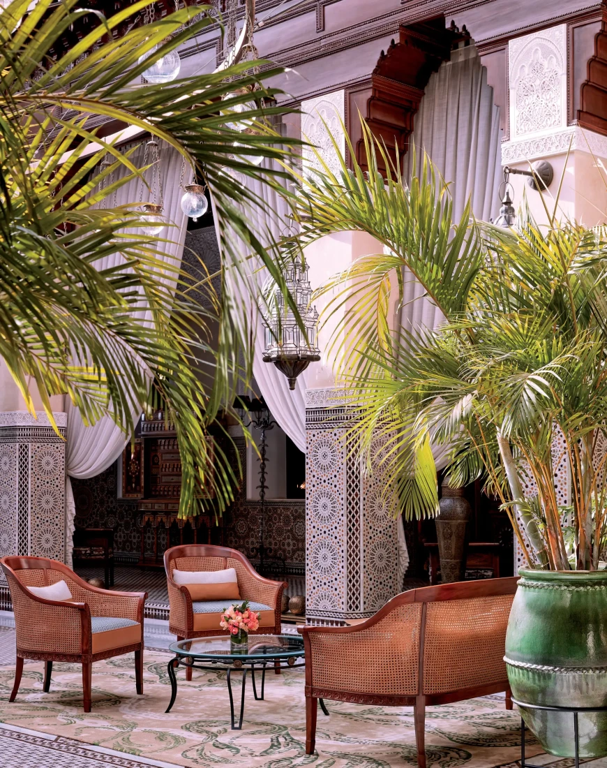 a couch and two chairs in an opulent courtyard filled with plants, curved arches, and intricate tile work