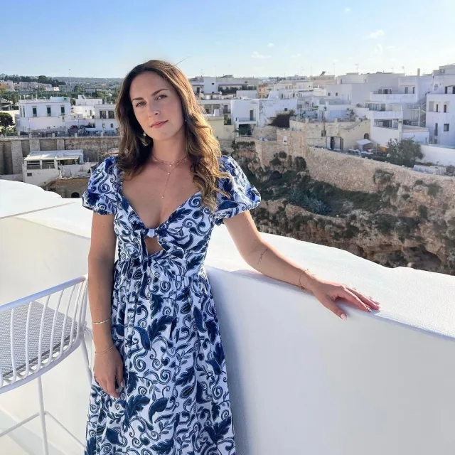 Picture of Brooke in a blue and white dress standing on a white patio in front of a grouping of white buildings 
