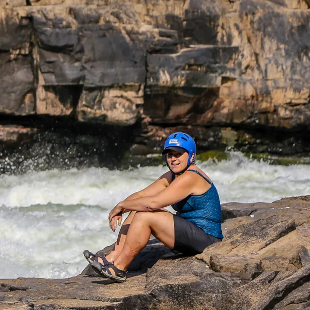 Heidi sitting on a rocks next to a rushing river. 