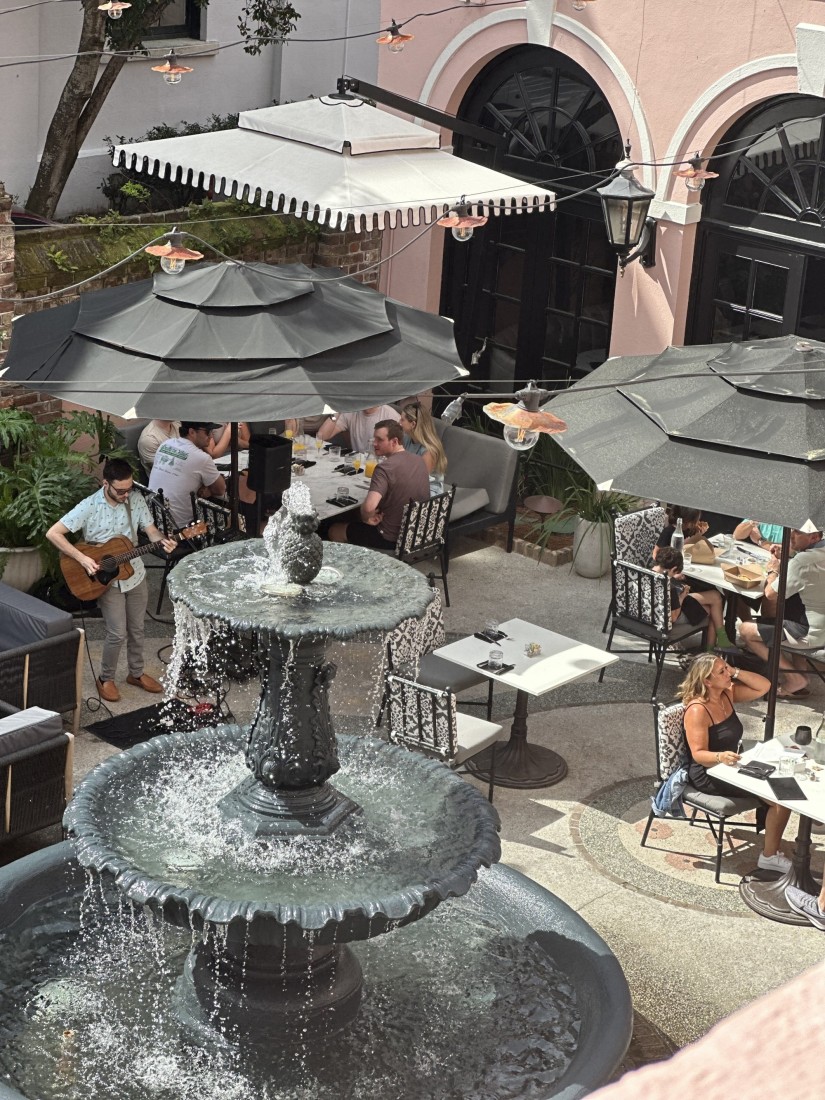 A view of a fountain and people dining on a patio with a person playing live music. 