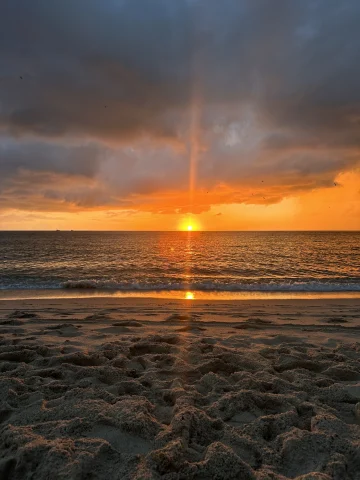 This is a serene and picturesque sunset at the beach. The sky is painted with hues of orange, yellow, and a touch of blue, indicating either dawn or dusk.
