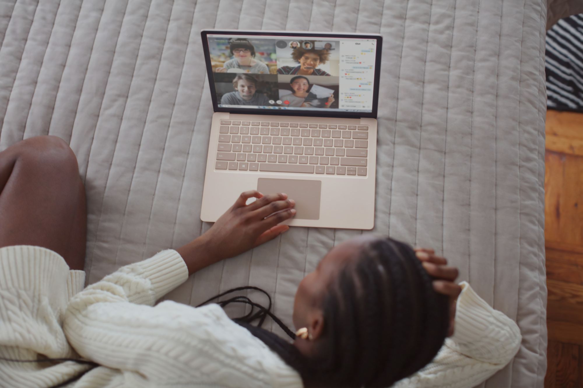 From a comfy position on her bed, a woman teleconferences on her PC