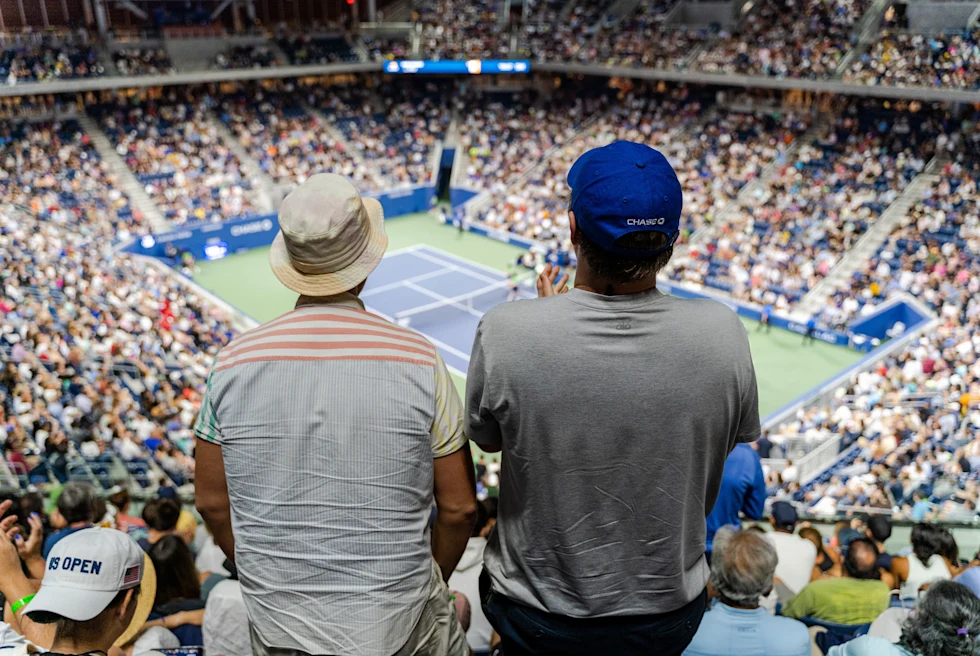 two people facing a tennis court in a crowded stadium