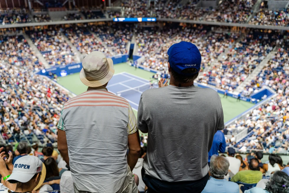 two people facing a tennis court in a crowded stadium