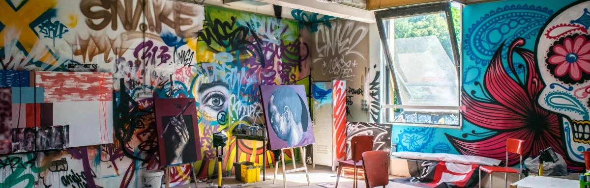 Inside gallery and open-space studio of street artist in France with colorful graffiti on walls and paintings displayed on easels.