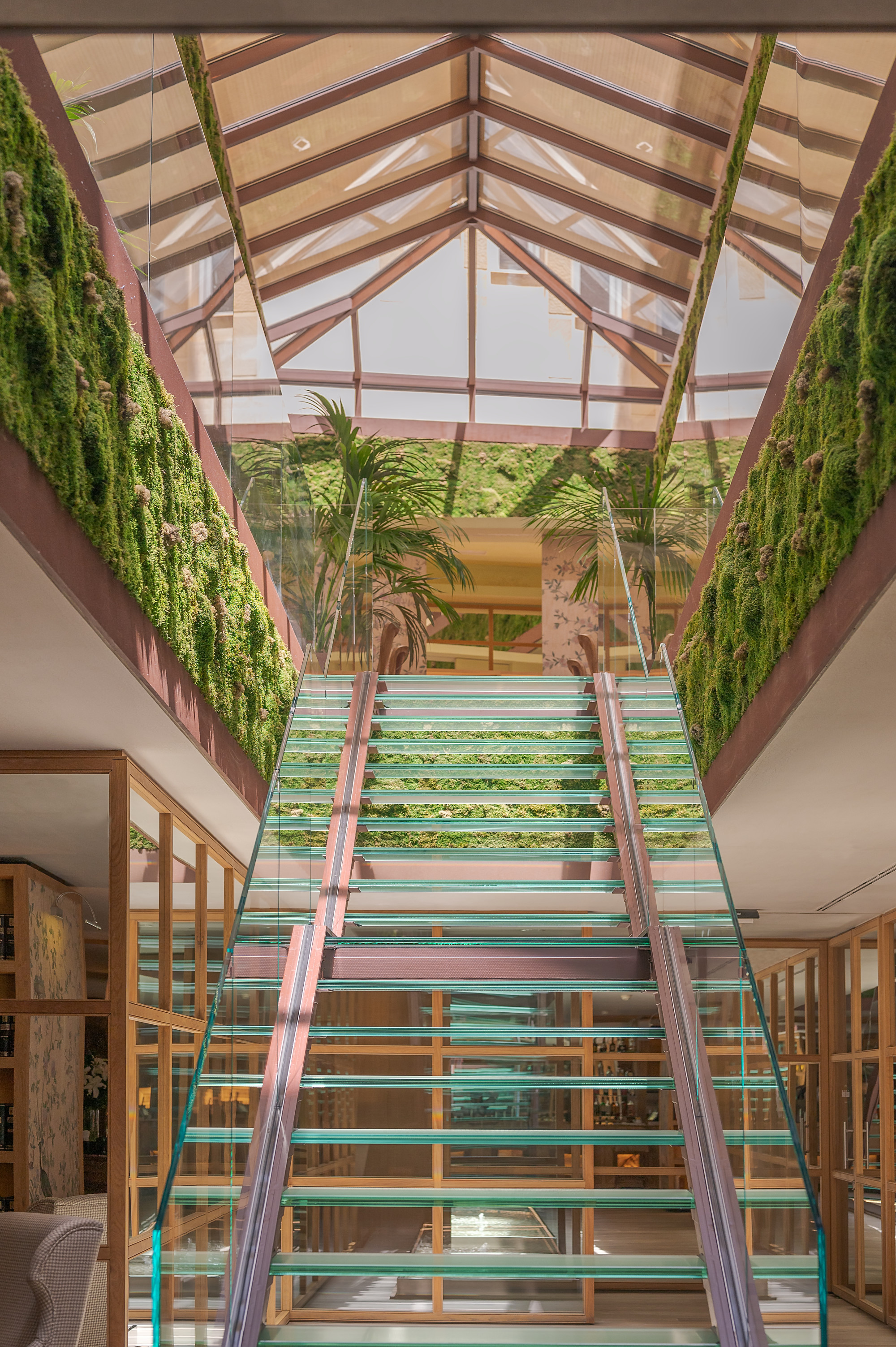 a glass staircase in a plant-filled lobby