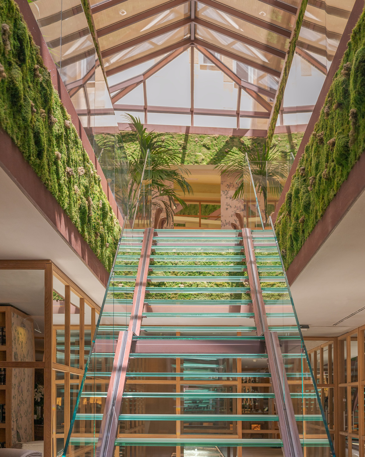 a glass staircase in a plant-filled lobby