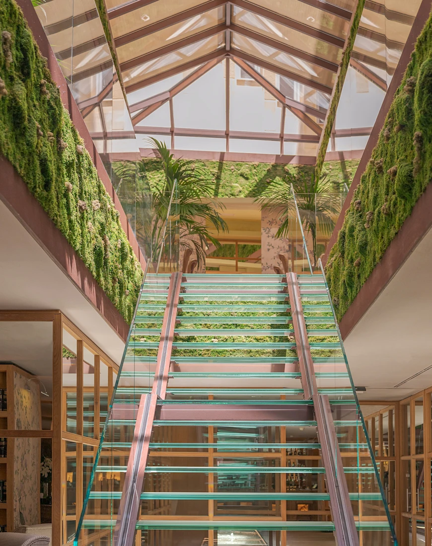a glass staircase in a plant-filled lobby