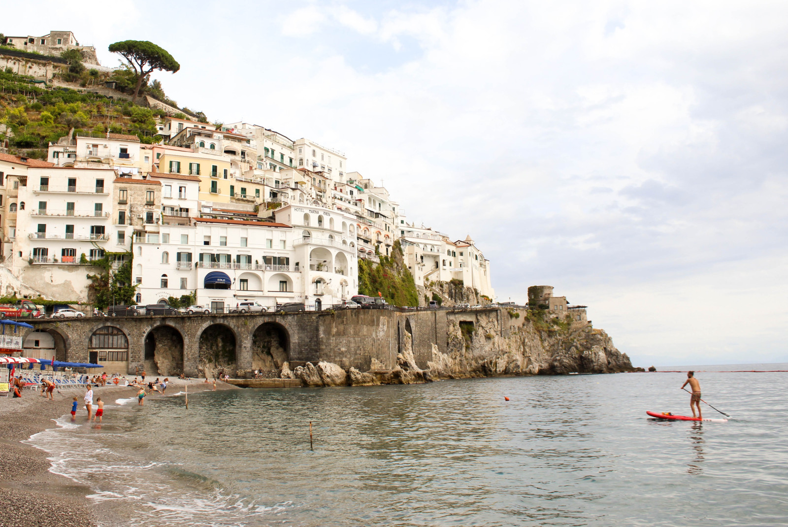 people on beach next to cliffs with buildings during daytime