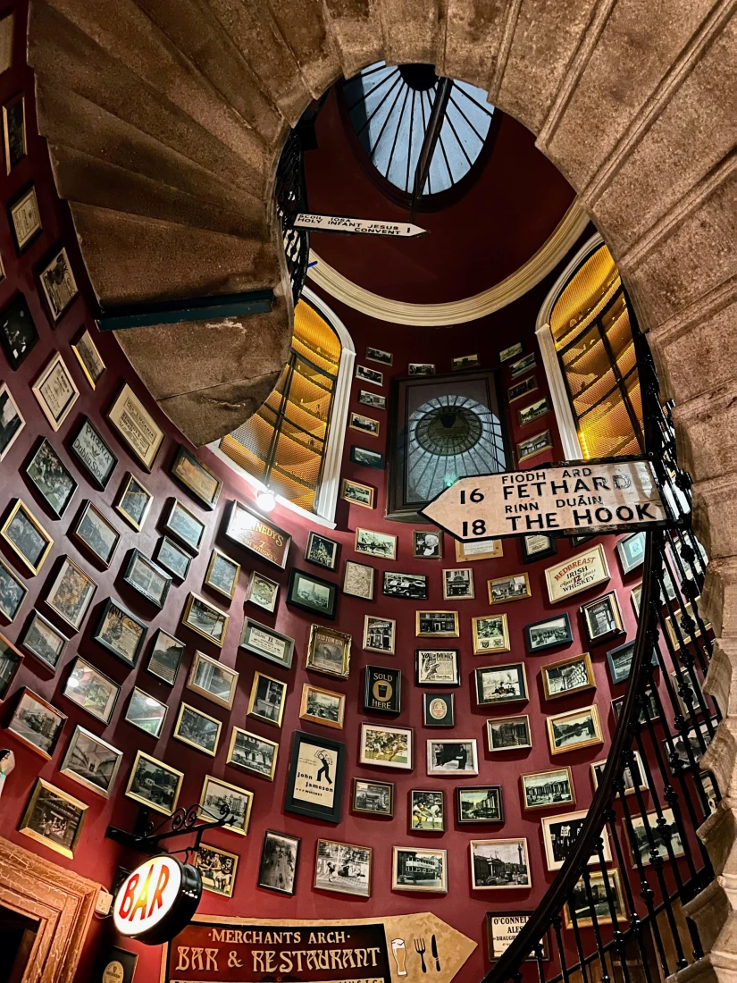 A photo of Merchants Arch Pub complete with a round staircase and framed photos lining the curved walls. 
