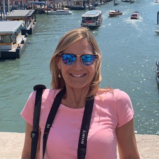 Fora travel agent wearing pink shirt and sunglasses with water in the background during daytime