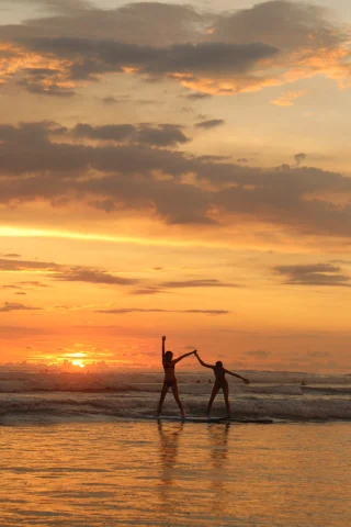 Two persons holding hands at beach during sunset.