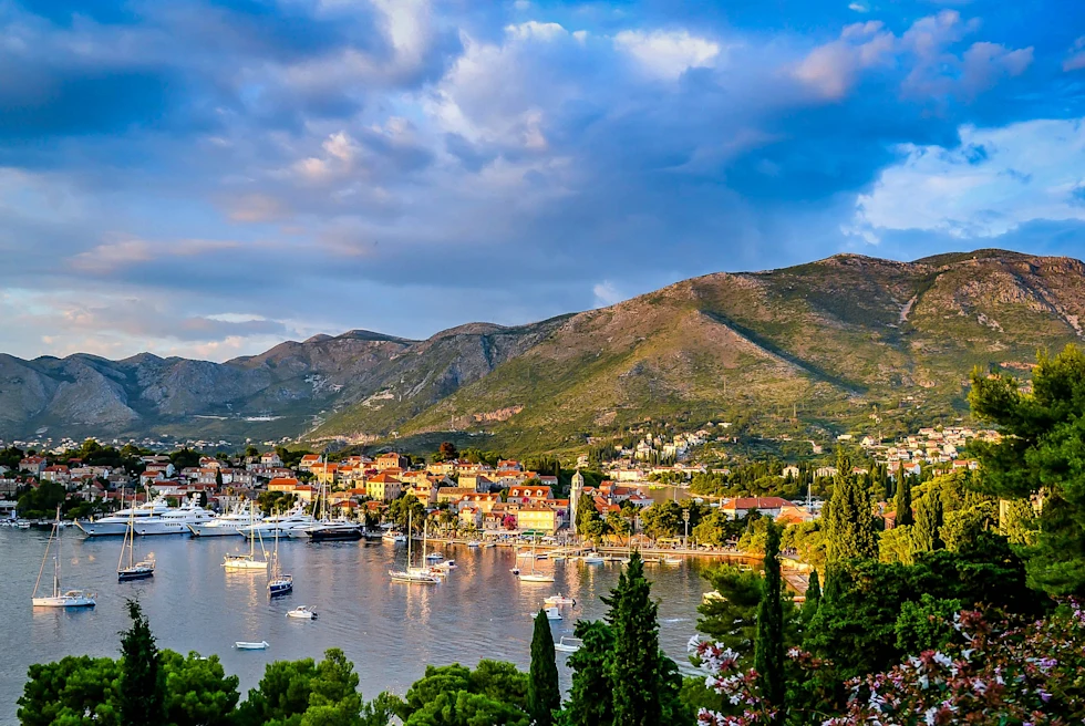 seaside historic town with a full harbor of boats, rolling hills in the distance, and blue sky with clouds.