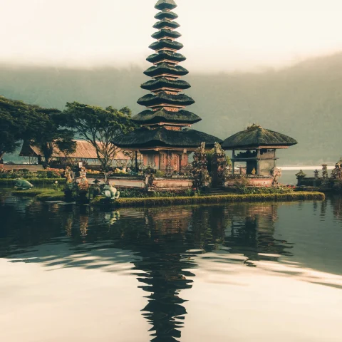 A picture of a temple beside a body of water and trees during daytime.