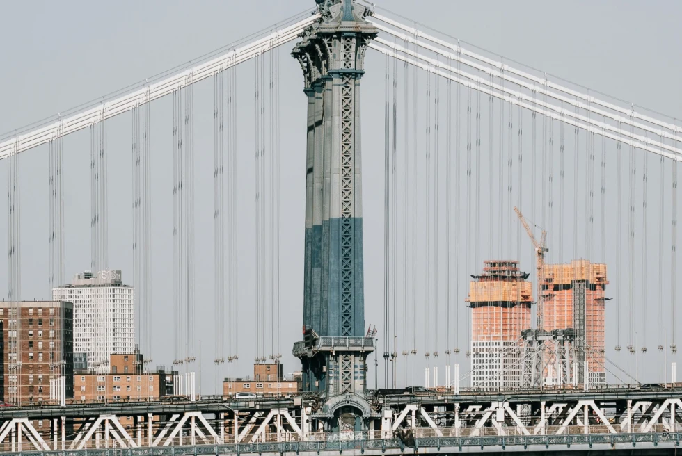 Grey bridge in front of brown city buildings.