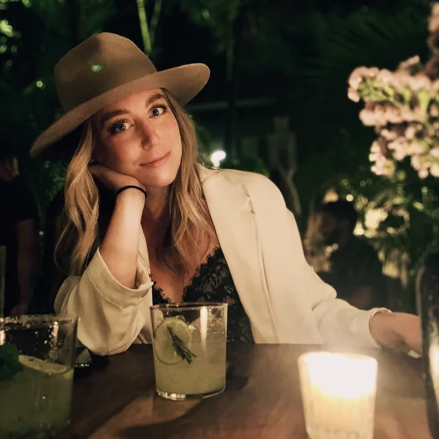 Travel advisor Katie Peters wearing brown hat and white jacket. Posing with her elbow on the table and a candle  in the view.