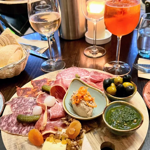 A charcuterie board on top of a table next to a glass of wine and Aperol Spritz. 