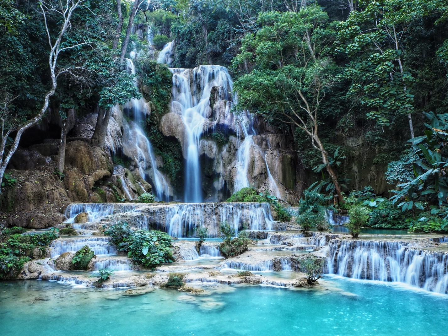 Roaring bright blue waterfalls surrounded green trees in Kuang Si Falls
