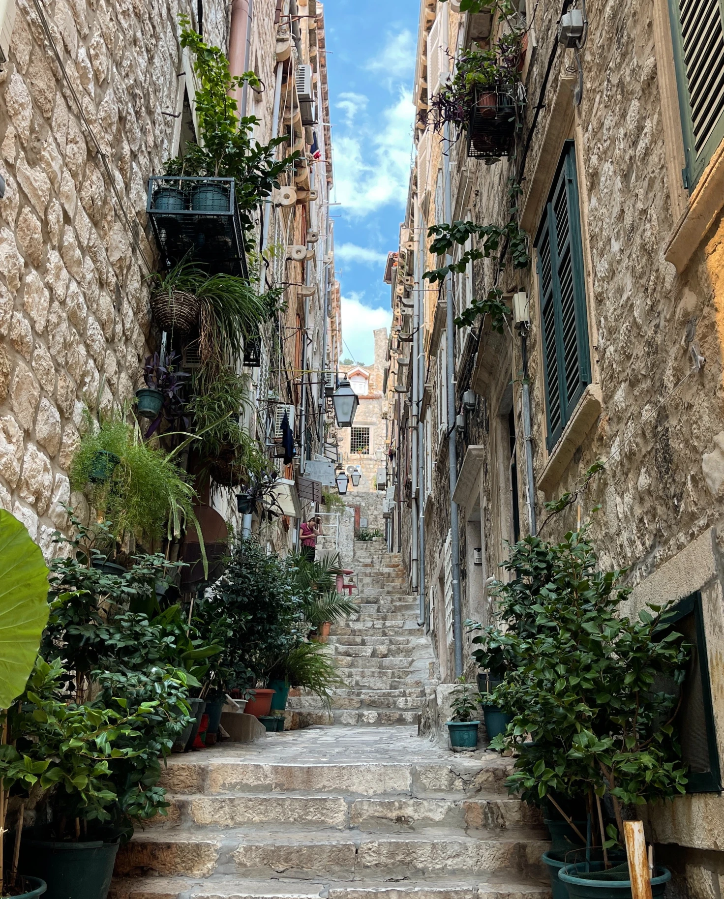 Narrow alleyway and stairway in Dubrovnik with plant pots and street lamps.