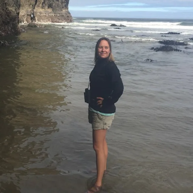 Travel Advisor Whitney Fessler in a black sweatshirt and khaki shorts standing on the beach.