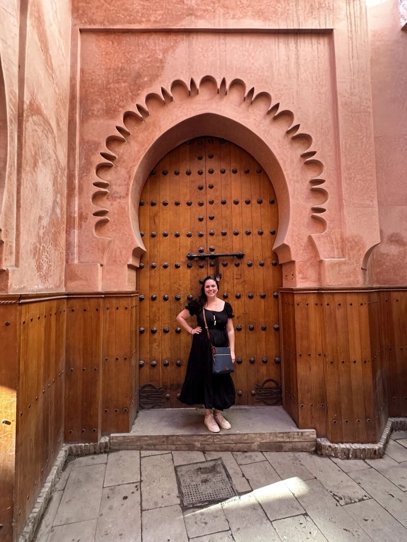 A person in a black dress posing for a photo in an arched doorway of a pink building