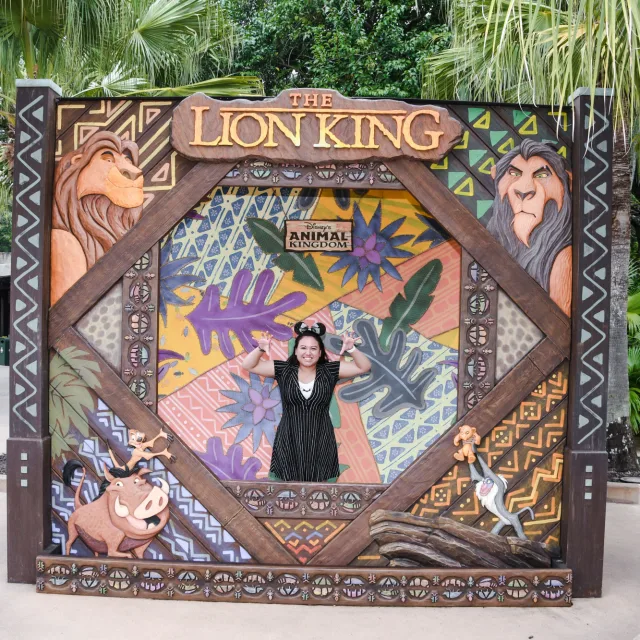 Travel Advisor Mayra Gonzalez stands inside a Lion King themed set at an amusement park surrounded by tropical trees