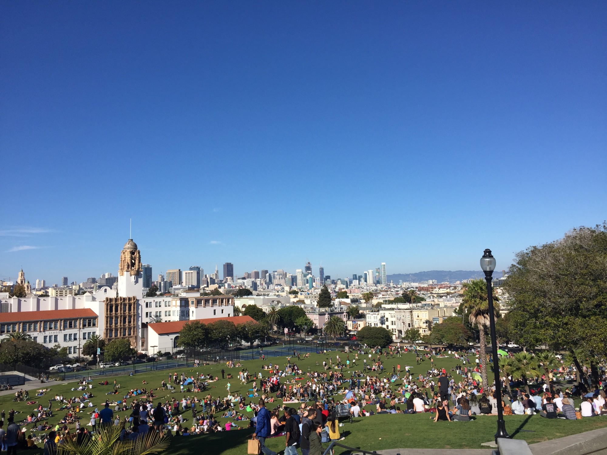 busy green park at the top of a hilly city with a clear blue sky