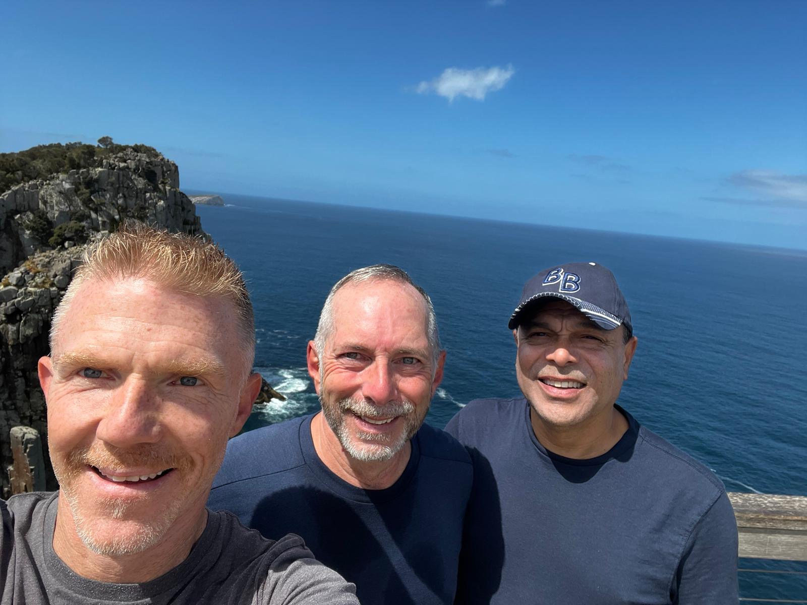 Three men with blue ocean in the background on a sunny day.