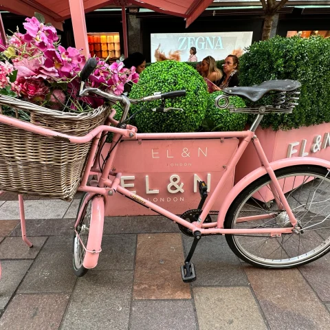 A small pink bicycle parked with pink pots. 