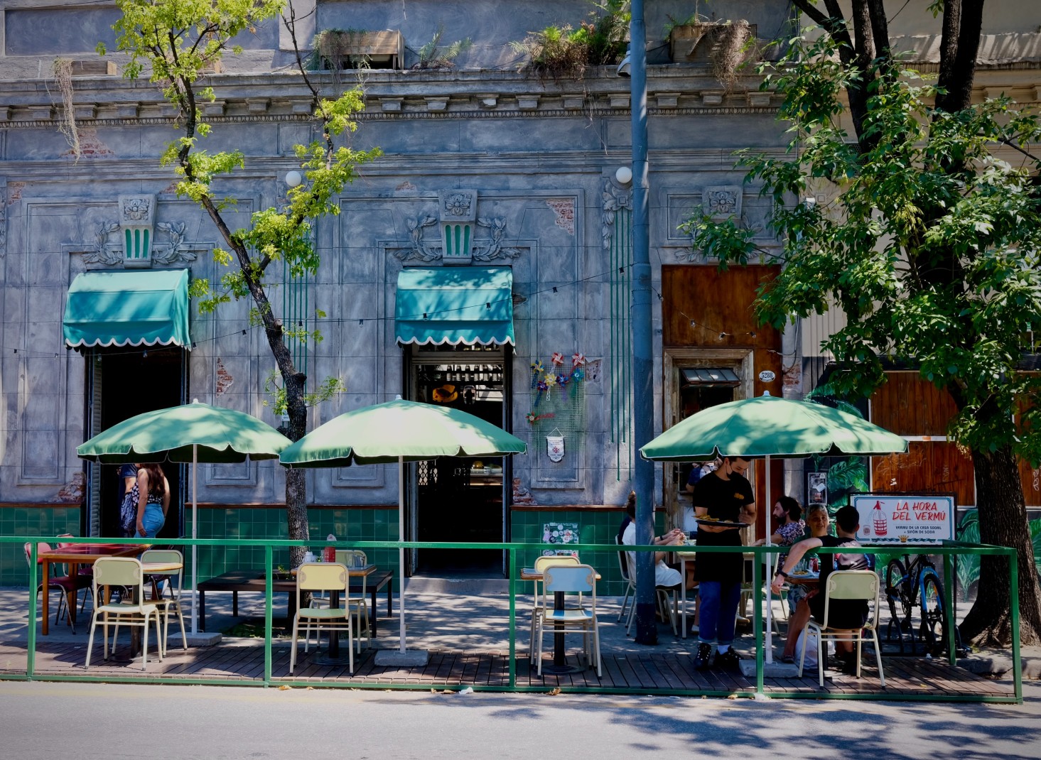 Green umbrellas and chairs on the sidewalk outside of a restaurant
