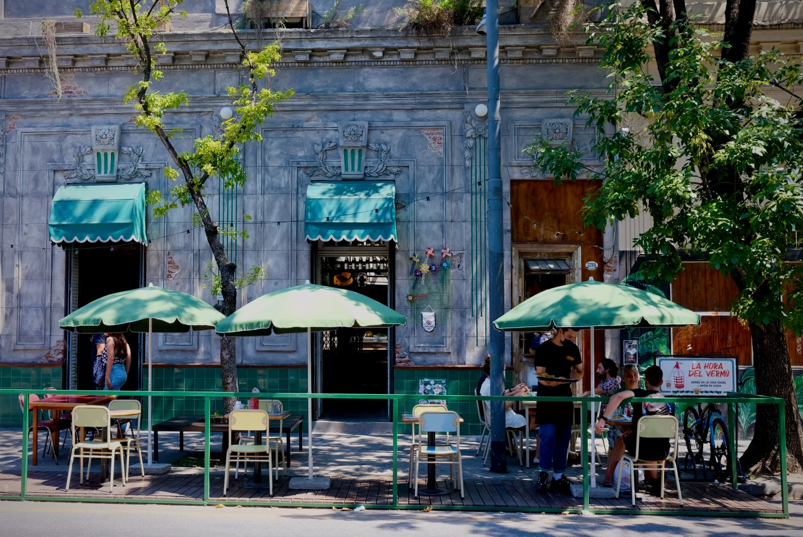 Green umbrellas and chairs on the sidewalk outside of a restaurant