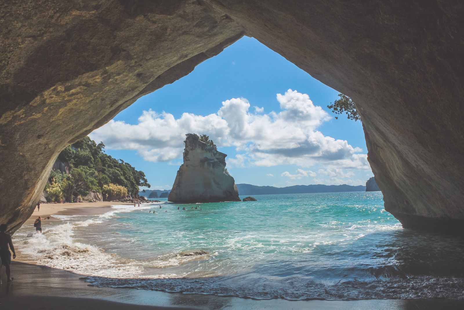 Cathedral Cove outside of Auckland, New Zealand with large rock formations in blue waters and a dark cave.
