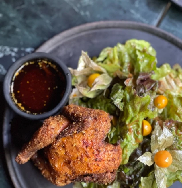 meal of fried chicken, salad and a dip on a black ceramic plate