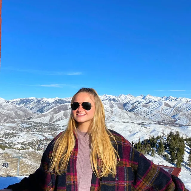 Travel Advisor Ally Pyne wears a tartan jacket and sunglasses in a snowy mountain range with clear blue sky
