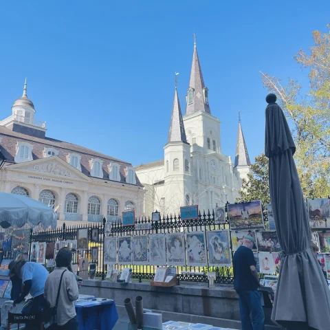 A bottom up view of old architecture, complete with pointed towers and a metal fence. There are also people and umbrellas in the forefront. 