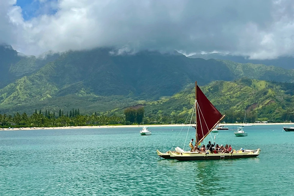 A beautiful view of the ocean with boats, clouds and stunning mountains in the distance.