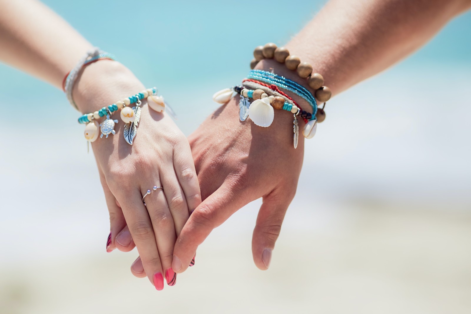 Two hands with blue bracelets with beach in background