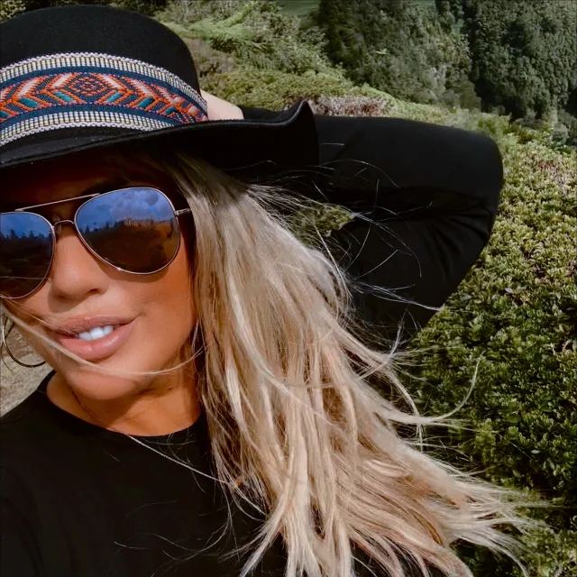 Travel advisor Sari Marissa Gower standing on a mountain peak wearing a black hat and aviator sunglasses.