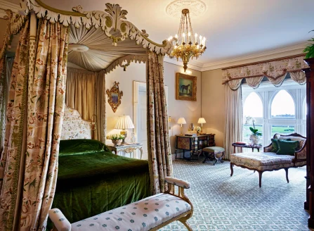 Ornate and regal hotel room with a canopy four-post bed with a green velvet bedspread and antique furniture