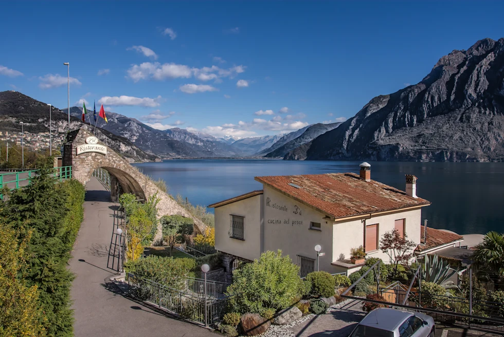 Lake Iseo views flanked by the Alps with a small rustic restaurant at the lake bank.