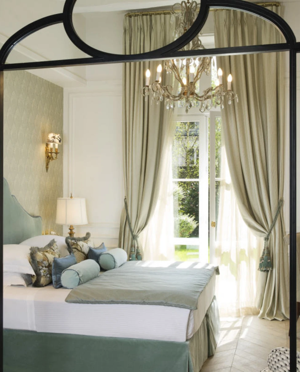 Charming French hotel room at the Relais Christine, in Paris, with a view of the garden through large, curtained windows.