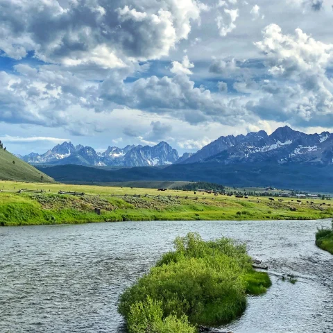 river surrounded by green fields with mountains in the background