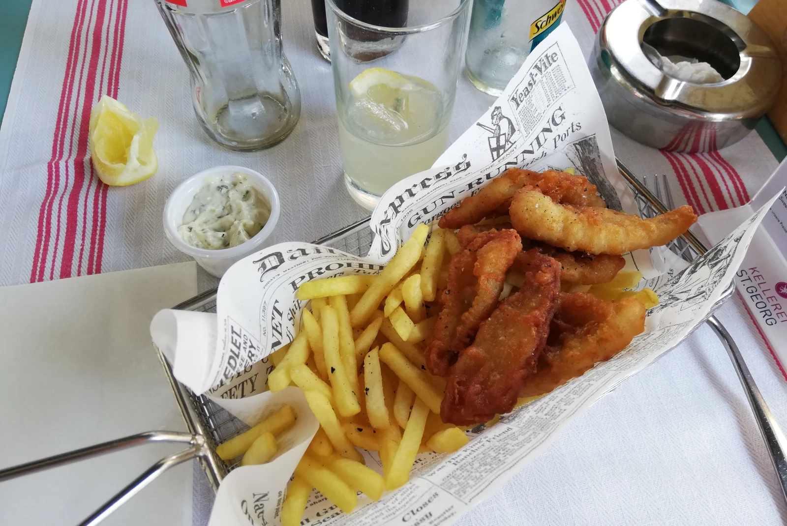 Fish and chips on a table next to lemonade. 